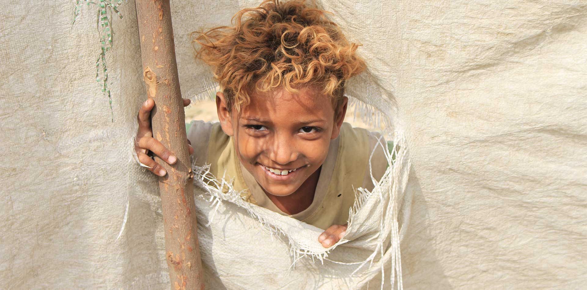 A displaced Yemeni child smiles from a torn tent